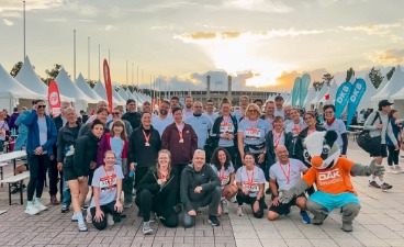 Team faw Berlin und BTZ Berlin beim B2Run Berlin 2026 Gruppenfoto der Läuferinnen und Läufer mit DAK-Maskottchen im Sonnenuntergang.